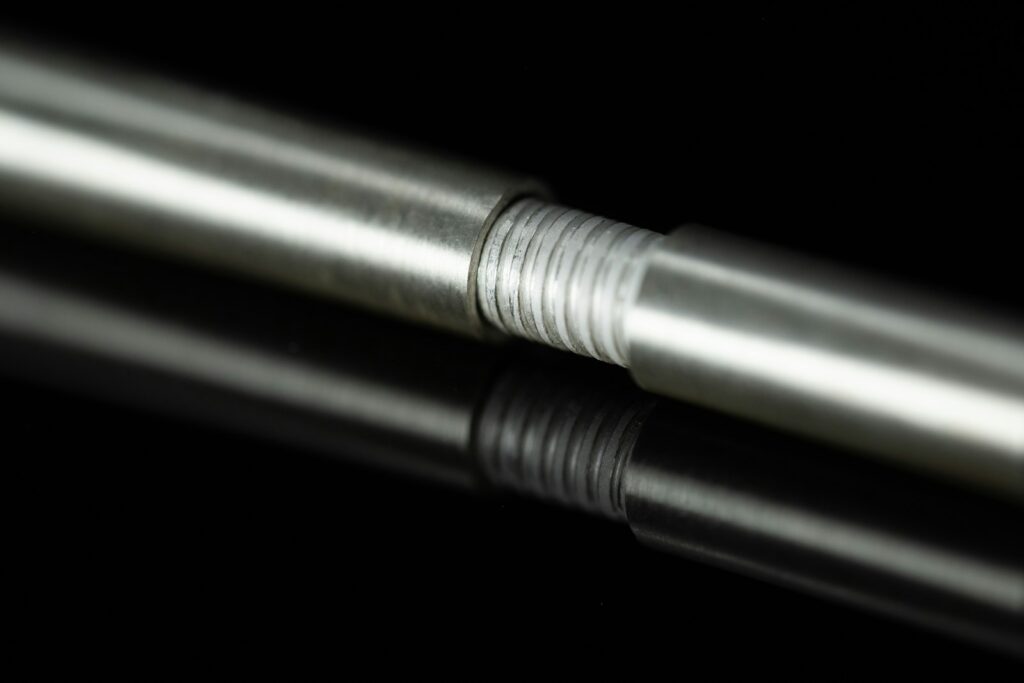 Threaded metal rod with a reflective finish resting on a black surface