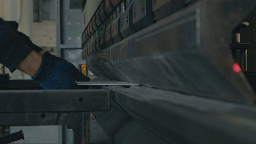 Worker's gloved hands positioning a metal sheet in a press brake bending machine