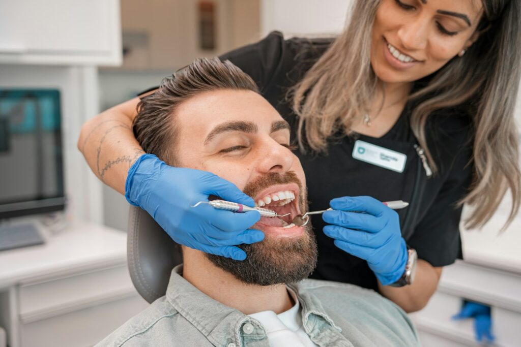 Dentist in blue gloves examining a man's teeth in a dental surgery during a check-up