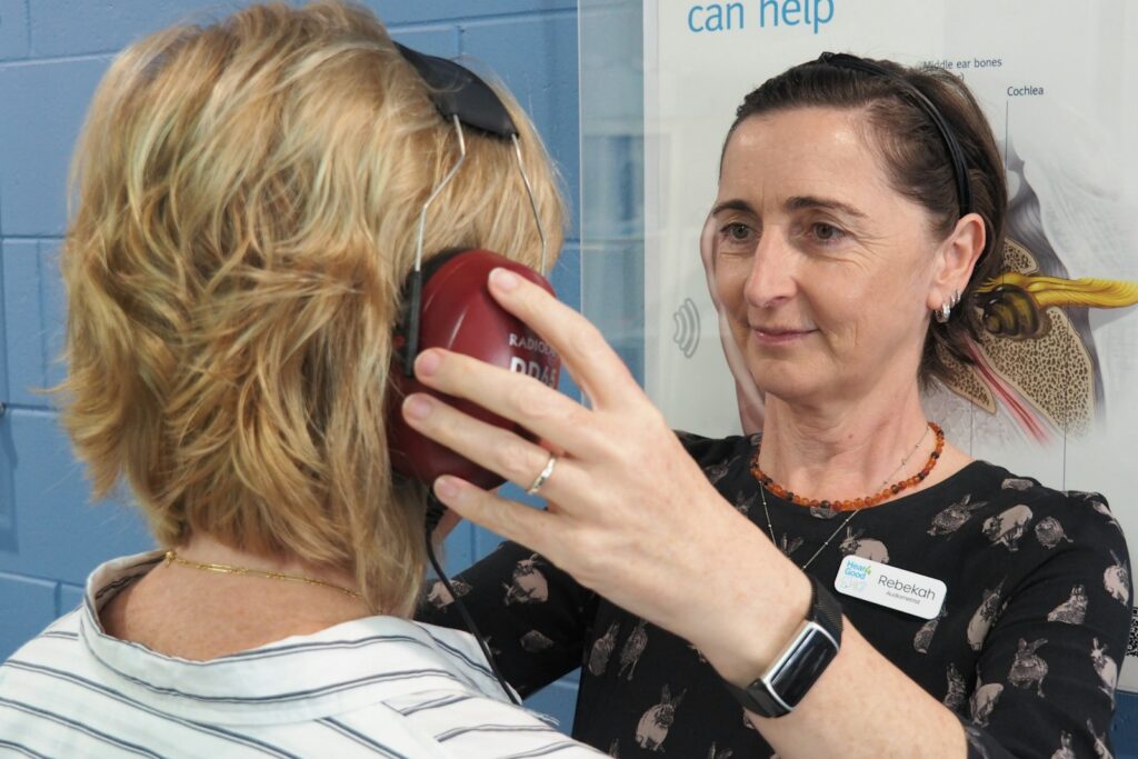 Audiologist helping a woman with a hearing test, with headphones placed on the client